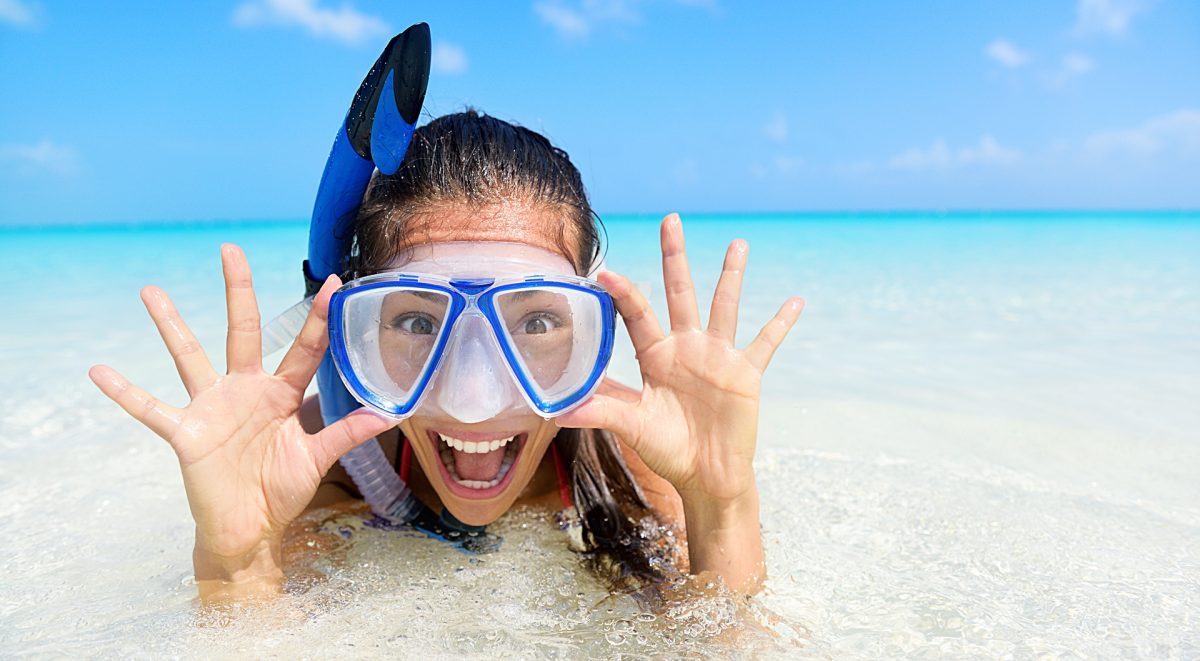 Beach vacation fun woman wearing a snorkel scuba mask making a goofy face while swimming in ocean water. Closeup portrait of Asian girl on her travel holidays. Summer or winter destination.